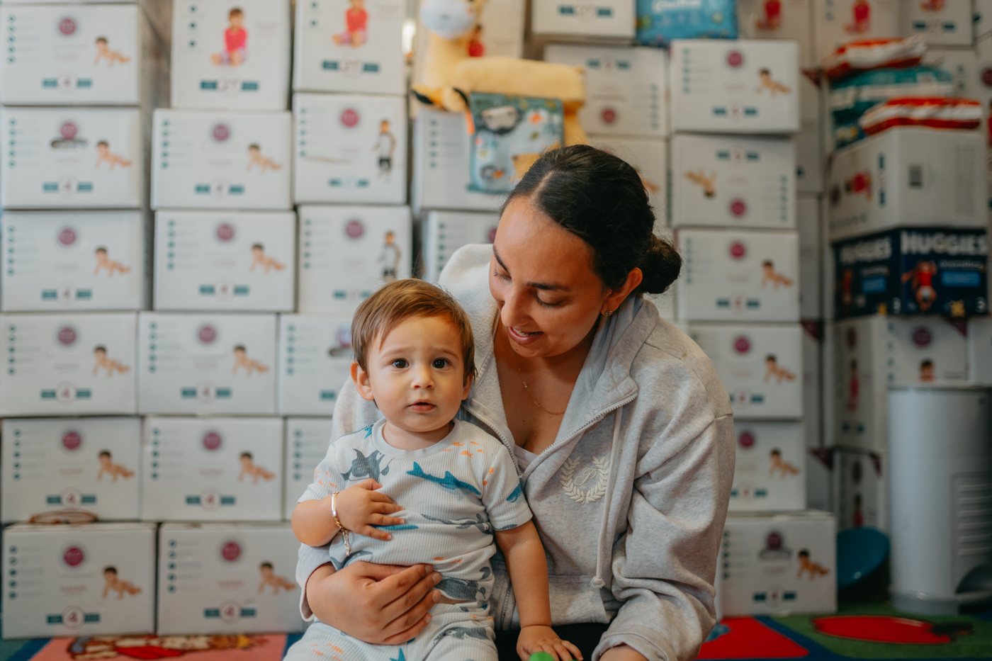 A parent holding their toddler in front of stacked Diaper Club boxes