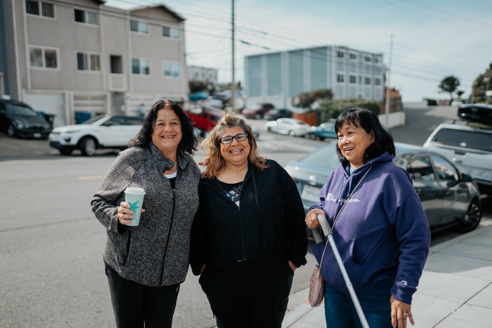 Three friends smiling together on a Daly City sidewalk