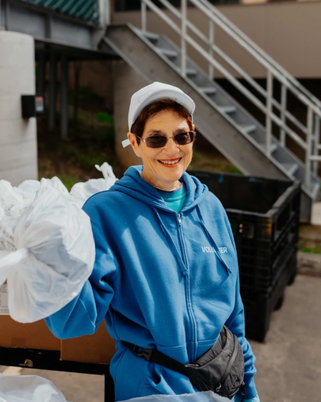 A smiling volunteer holding bags at the weekly food distribution